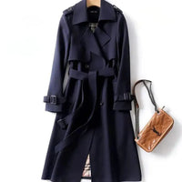 Classic navy trench coat with a belted waist, button details, and shoulder epaulets, paired with a tan quilted handbag. Perfect for timeless style.