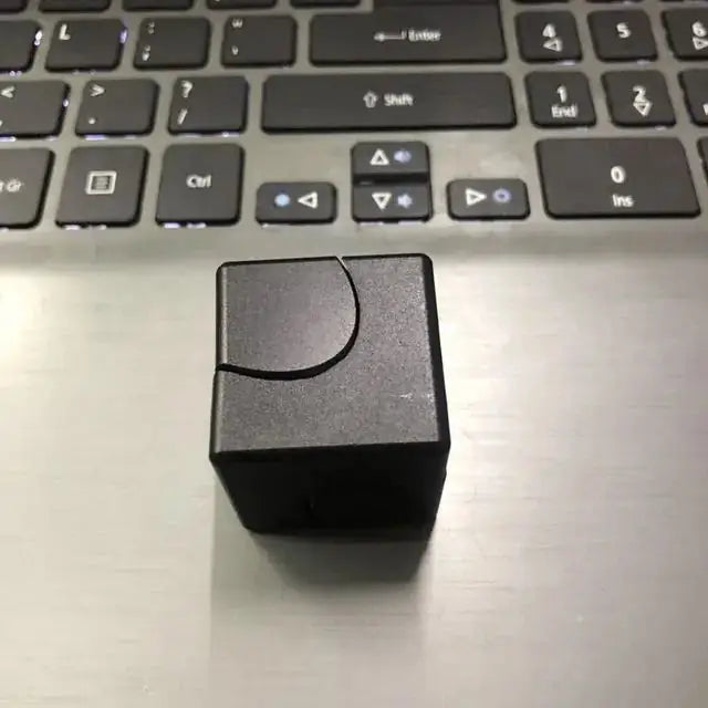 Black metallic fidget spinner cube on a laptop, featuring a minimalist design for stress relief and focus improvement.
