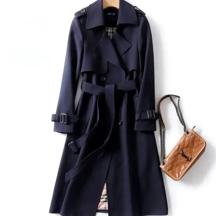 Classic navy trench coat with a belted waist, double-breasted design, and shoulder epaulets, paired with a tan quilted handbag.