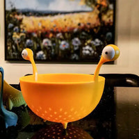 OTOTO Draining Basket for Kitchen on a counter with light filtering through its holes, emphasizing its whimsical design and space-saving feet.