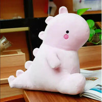 Pink dinosaur plush toy with a cute and cuddly appearance, placed on a wooden desk with books and plants nearby.