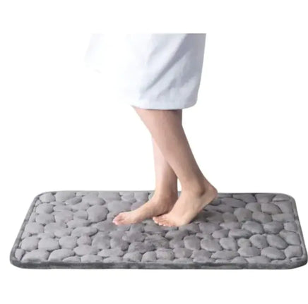 Gray super absorbent shower room floor mat with a pebble-like texture, shown with a person stepping on it.