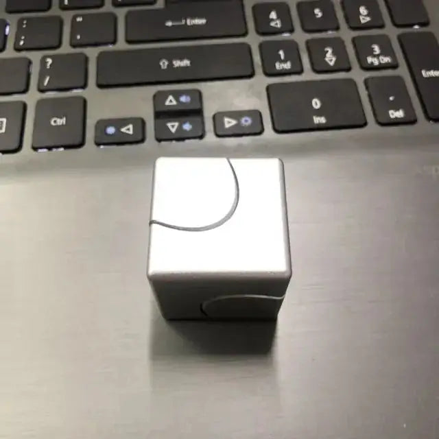 Silver metallic fidget spinner cube on a laptop, showcasing its sleek and minimalist design for stress relief.