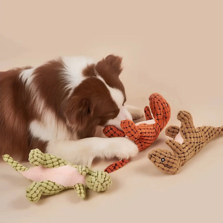 Dog playing with a set of dinosaur plush toys in green, orange, and brown, perfect for chewing and interactive fun.