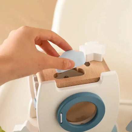 Close-up of a hand placing a blue shape into the wooden educational rocket toy, promoting fine motor skills and creativity.